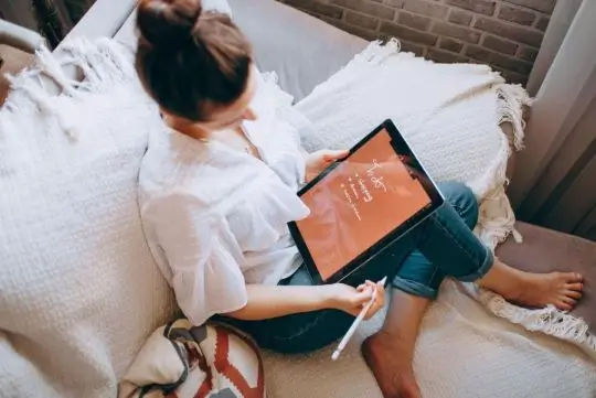 Person using a tablet with a notebook and pen nearby—illustrating intentional use of digital tools for clarity, planning, and productivity.