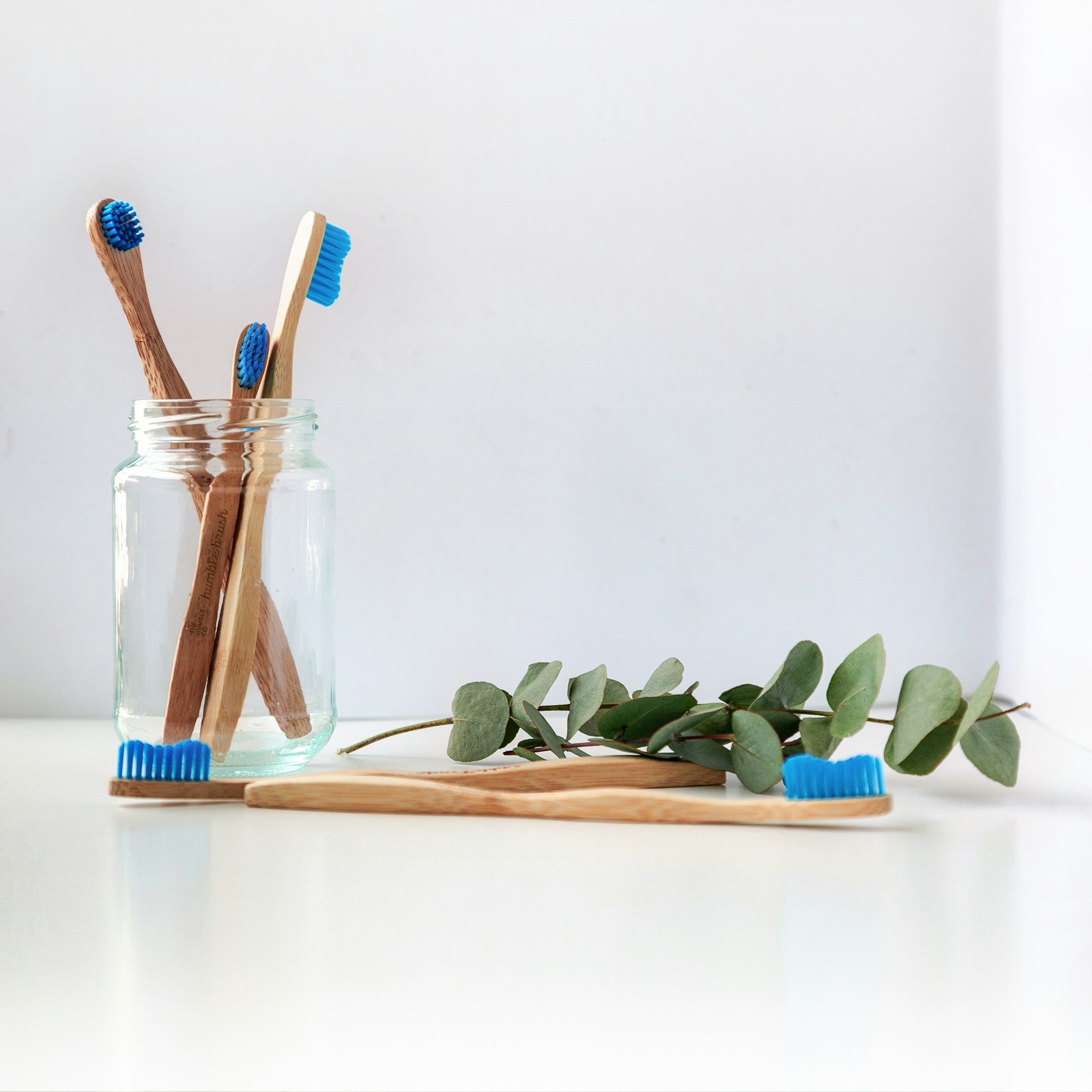 Four bamboo toothbrushes lined up on a folded white linen towel in soft natural light, each handle slightly different in shape and color