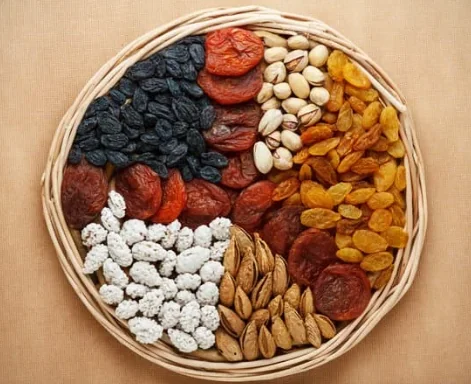 Round wicker basket filled with a colorful assortment of dried fruits and nuts (apricots, raisins, pistachios, almonds).