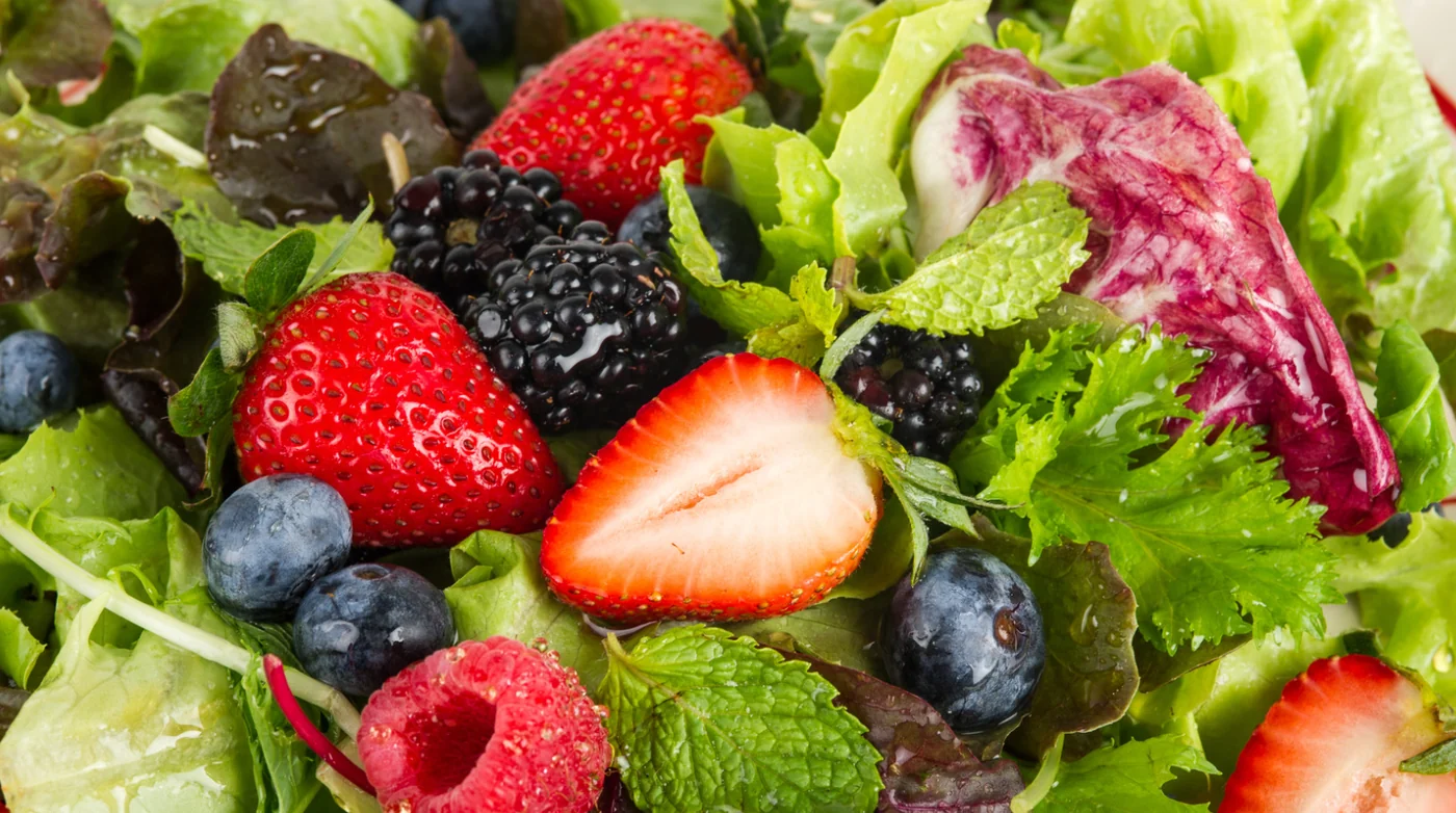 Close-up of a fresh fruit salad with strawberries, blueberries, raspberries, blackberries and leafy greens.
