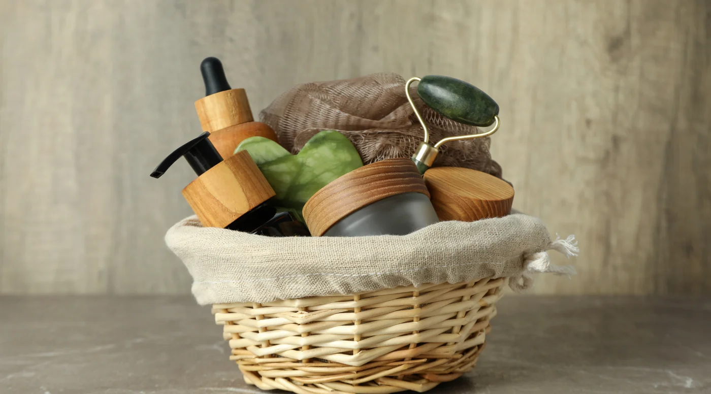 Spa skincare set in a woven basket with wooden-cap bottles, a jade roller, loofah, and beige fabric lining.